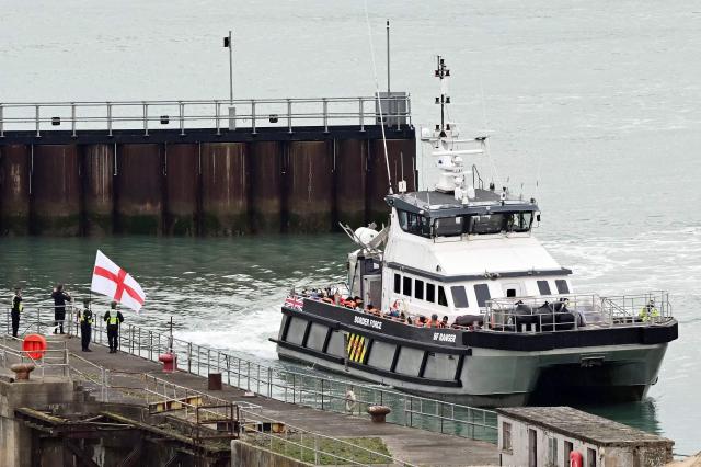 CORRECTION / A man waves a St George's cross England flag as a British Border Force vessel carrying migrants picked up at sea, while attempting to cross the English Channel from France, arrives into the Port of Dover in southeast England, on April 01, 2026.  (Photo by JUSTIN TALLIS / AFP) / “The erroneous mention[s] appearing in the metadata of this photo by JUSTIN TALLIS has been modified in AFP systems in the following manner: The location should read [Dover, Kent, Unitd Kingdom] instead of [Dover, Delaware, USA]. Please immediately remove the erroneous mention[s] from all your online services and delete it (them) from your servers. If you have been authorized by AFP to distribute it (them) to third parties, please ensure that the same actions are carried out by them. Failure to promptly comply with these instructions will entail liability on your part for any continued or post notification usage. Therefore we thank you very much for all your attention and prompt action. We are sorry for the inconvenience this notification may cause and remain at your disposal for any further information you may require.”