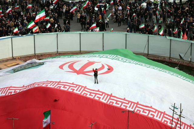 A boy raises his fist while standing on a giant Iranian flag during the funeral of Alireza Tangsiri, commander of the Iranian Revolutionary Guards' navy alongside others killed in US-Israeli strikes on Iran at Enghelab Square in Tehran on April 1, 2026. Iran confirmed on March 30 that an Israeli strike had killed the commander of the naval force of the Revolutionary Guards, who Israel had said was responsible for the blocking of the Strait of Hormuz. A statement carried by the Guards' Sepah News website said Alireza Tangsiri "succumbed to severe injuries" from the attack last week. (Photo by AFP) / 