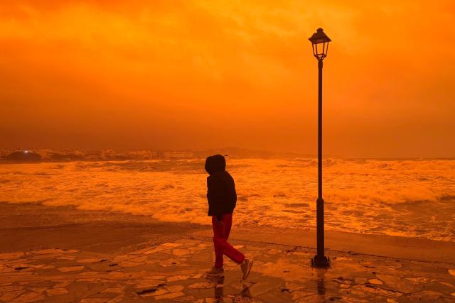 A locql resident walks on the port of Ierapetra during a dust storm on the Greek island of Crete on April 1, 2026. (Photo by Eleftherios Elis / AFP)