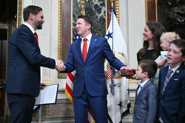 (L/R) US Vice President JD Vance shakes hands with Colin McDonald as Assistant Attorney General for the National Fraud Enforcement Division after swearing him in as McDonald's wife Janessa holds the Bible in the Eisenhower Executive Office Building, next to the White House in Washington, DC on April 1, 2026. McDonald will be the first Assistant Attorney General for the Department of Justice's newly created National Fraud Enforcement Division. (Photo by Mandel NGAN / AFP)