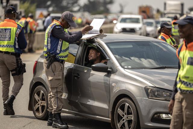 A Johannesburg Metro Police Department (JMPD) officer issues a fine to a driver during a roadblock near Johannesburg on April 1, 2026. (Photo by EMMANUEL CROSET / AFP)