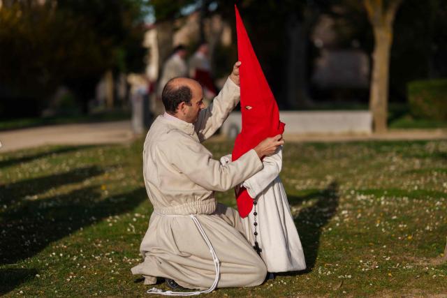TOPSHOT - A young member of the "Real Hermandad del Santisimo Cristo de las Injurias" brotherhood gets a hood positioned while getting dressed before taking part in the Holy Wednesday Silence Procession in Zamora, northwestern Spain, on April 1, 2026. Spain's colourful Holy Week celebrations started this week, featuring centuries-old processions of the faithful carrying flower-covered floats topped with statues of Christ or the Virgin Mary that draw huge crowds. Organised by various religious brotherhoods, or "confradias", the parades are held across the country in the week leading up to Easter Sunday, which this year in the Roman Catholic Church falls on April 5, 2026. (Photo by CESAR MANSO / AFP)