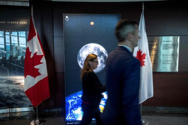 People walk past an image of the moon at the Canadian Space Agency (CSA) before a viewing party of the Artemis II launch, in Longueuil, near Montreal, Quebec, on April 1, 2026. Three men and one woman are set to embark on the first crewed journey to the Moon since 1972, a landmark odyssey that aims to launch the US into a new era of space exploration. The NASA mission dubbed Artemis II has been years in the making after facing repeated setbacks, but is finally scheduled to take off from Florida as early as April 1 at 6:24 pm (2224 GMT). (Photo by ANDREJ IVANOV / AFP)