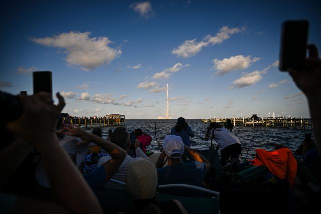 TOPSHOT - Space enthusiasts at a park in Titusville, view the Artemis II crewed lunar mission lift off from Pad 39B at Kennedy Space Center in Cape Canaveral, Florida, on April 1, 2026. Four astronauts blasted off aboard a massive NASA rocket April 1 on a long-anticipated journey around the Moon, the first crewed lunar flyby in more than 50 years. With an intense roar that reverberated far beyond the launchpad, the enormous orange-and-white rocket carried three Americans and one Canadian away from Florida's Kennedy Space Center at approximately 6:35 pm local time, according to an AFP journalist onsite. "We're going to the Moon!" yelled a spectator. (Photo by Miguel J Rodriguez Carrillo / AFP)