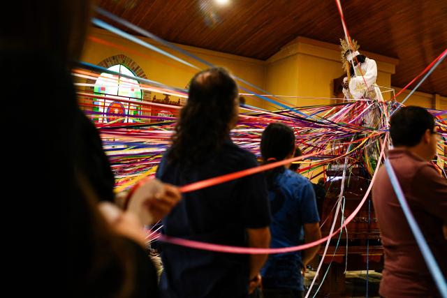 Catholic faithful hold colored tape tied to a statue of Jesus Christ as they take part in a mass at the San Antonio de Padua church, ahead of a procession known as "Jesus Nazareno of the tapes," during the Holy Week in Cartago, Costa Rica on April 1, 2026. (Photo by Ezequiel BECERRA / AFP)