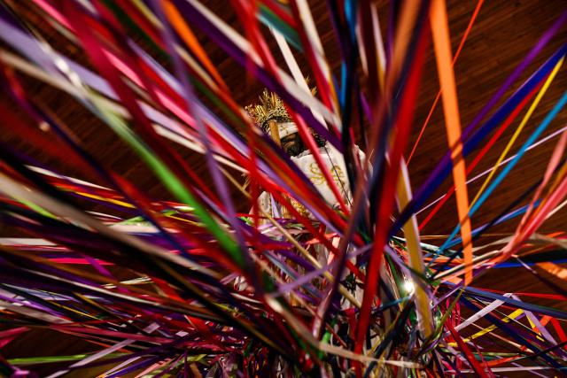 Catholic faithful hold colored tape tied to a statue of Jesus Christ as they take part in a mass at the San Antonio de Padua church, ahead of a procession known as "Jesus Nazareno of the tapes," during the Holy Week in Cartago, Costa Rica on April 1, 2026. (Photo by Ezequiel BECERRA / AFP)