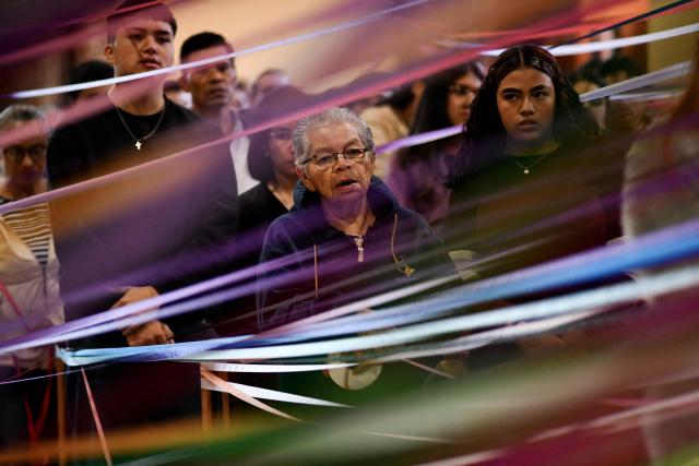 Catholic faithful hold colored tape tied to a statue of Jesus Christ as they take part in a mass at the San Antonio de Padua church, ahead of a procession known as "Jesus Nazareno of the tapes," during the Holy Week in Cartago, Costa Rica on April 1, 2026. (Photo by Ezequiel BECERRA / AFP)