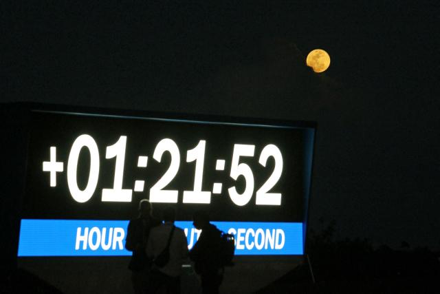 A full moon rises above the mission clock after NASA's Artemis II Space Launch System (SLS) rocket and Orion spacecraft successfully lifted off from the Kennedy Space Center in Cape Canaveral, Florida on April 1, 2026. Four astronauts blasted off aboard a massive NASA rocket April 1 on a long-anticipated journey around the Moon, the first crewed lunar flyby in more than 50 years. With an intense roar that reverberated far beyond the launchpad, the enormous orange-and-white rocket carried three Americans and one Canadian away from Florida's Kennedy Space Center at approximately 6:35 pm local time, according to an AFP journalist onsite. "We're going to the Moon!" yelled a spectator. (Photo by Gregg Newton / AFP)