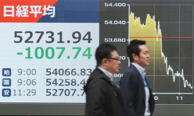 Passersby walk past electronic quotation boards displaying the Nikkei Stock Average on the Tokyo Stock Exchange (L) along a street in Tokyo on April 2, 2026. (Photo by Kazuhiro NOGI / AFP)