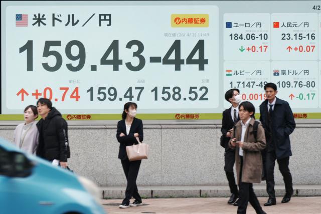 Passersby stand in front of electronic quotation boards displaying the foreign exchange rate of the Japanese yen against the US dollar (L) and other major foreign currencies along a street in Tokyo on April 2, 2026. (Photo by Kazuhiro NOGI / AFP)