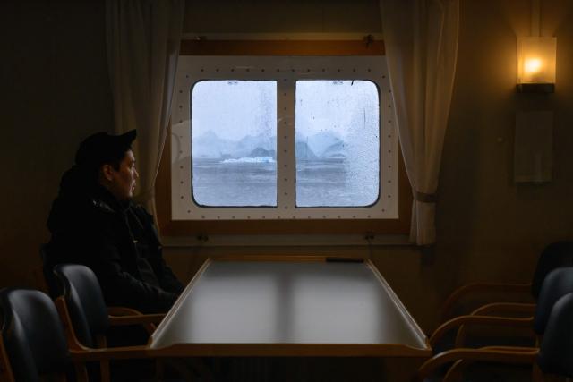 A man watches, from a porthole in the canteen, icebergs drifting through the Icefjord toward Ilulissat, Greenland, on March 15, 2026. The Sarfaq Ittuk is a vital and iconic coastal ferry for Greenlanders, keeping small west coast communities connected to low cost. It links Qaqortoq in the south to Ilulissat in the north in a week-long journey. This year, an unusually warm January allowed the ferry to reach Ilulissat much earlier than usual, as the town is normally blocked by sea ice in March. Around 200 passengers travel on board for medical needs, work, tourism, or simply to meet people. But with new airports opening and a lack of investors, the future of the Sarfaq Ittuk is increasingly uncertain. (Photo by Florent VERGNES / AFP)