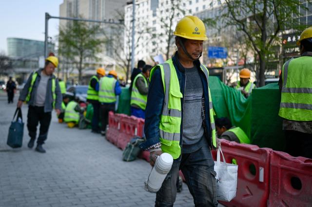 A group of workers spend their lunch time along a road in Beijing on April 2, 2026. (Photo by WANG Zhao / AFP)