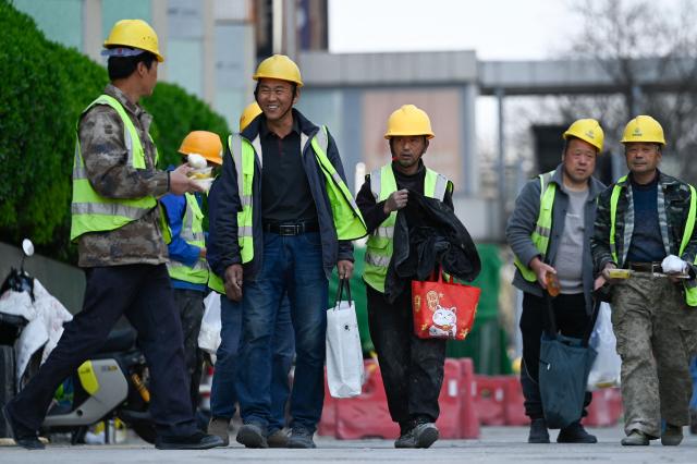 A group of workers spend their lunch time along a road in Beijing on April 2, 2026. (Photo by WANG Zhao / AFP)