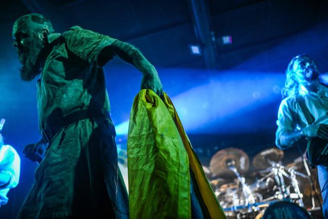 The frontman of the Ukrainian metal band "1914" Dmytro Ternushchak, with the stage name "Kumar", holds a Ukrainian national flag as he performs on stage during a concert at the Proxima music club in Warsaw on March 25, 2026. Like other bands, "1914" is raising money for the Ukrainian army. Kumar is attempting to "open the eyes" of Europeans in light of the Kremlin's warmongering, showing that Ukraine poses as an "eastern shield". Their latest album, released in November 2025, follows the story of a Ukrainian from Galicia in their fight against Russia in the First World War. (Photo by Sergei GAPON / AFP)