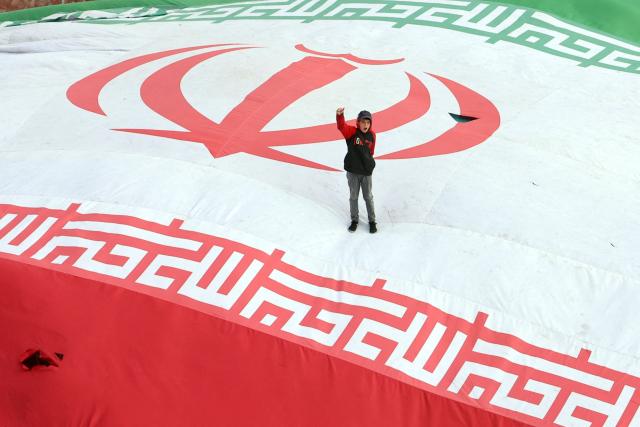 TOPSHOT - A boy raises his fist while standing on a giant Iranian flag during the funeral of Alireza Tangsiri, commander of the Iranian Revolutionary Guards' navy, alongside others killed in US-Israeli strikes on Iran at Enghelab Square in Tehran on April 1, 2026. Iran confirmed on March 30 that an Israeli strike had killed the commander of the naval force of the Revolutionary Guards, who Israel had said was responsible for the blocking of the Strait of Hormuz. A statement carried by the Guards' Sepah News website said Alireza Tangsiri "succumbed to severe injuries" from the attack last week. (Photo by AFP) / ALTERNATIVE CROP
