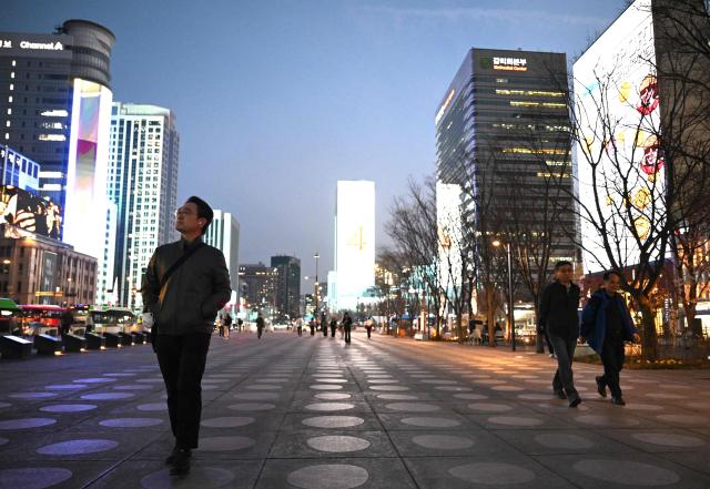 People walk in front of digital billboards at Gwanghwamun Square in Seoul on April 1, 2026. Hopes of making downtown Seoul dazzle more than Times Square have hit a setback with new guidelines to dim the massive digital billboards that light up the South Korean capital after a barrage of complaints. (Photo by Jung Yeon-je / AFP)