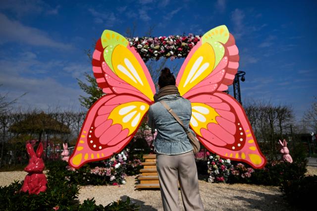 A woman stands in front of a butterfly decoration at the 'Gertrudenhof' adventure farm for children in Huerth, western Germany on April 2, 2026, ahead of the Easter celebrations. (Photo by Ina FASSBENDER / AFP)
