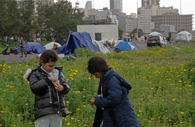 Displaced girls pluck flowers near their tents at an unofficial camp for displaced people on Beirut's waterfront area on April 2, 2026. Lebanon was drawn into the Middle East war on March 2 when Tehran-backed militant group Hezbollah launched attacks on Israel to avenge the killing of the Iranian leader. Israel has responded with broad strikes across Lebanon and a ground offensive. (Photo by Joseph EID / AFP)