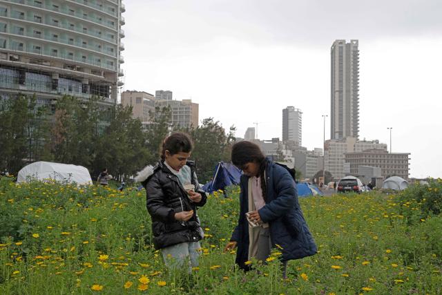 Displaced girls pluck flowers near their tents at an unofficial camp for displaced people on Beirut's waterfront area on April 2, 2026. Lebanon was drawn into the Middle East war on March 2 when Tehran-backed militant group Hezbollah launched attacks on Israel to avenge the killing of the Iranian leader. Israel has responded with broad strikes across Lebanon and a ground offensive. (Photo by Joseph EID / AFP)