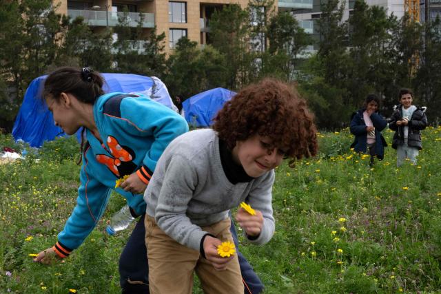 Displaced girls pluck flowers near their tents at an unofficial camp for displaced people on Beirut's waterfront area on April 2, 2026. Lebanon was drawn into the Middle East war on March 2 when Tehran-backed militant group Hezbollah launched attacks on Israel to avenge the killing of the Iranian leader. Israel has responded with broad strikes across Lebanon and a ground offensive. (Photo by Joseph EID / AFP)