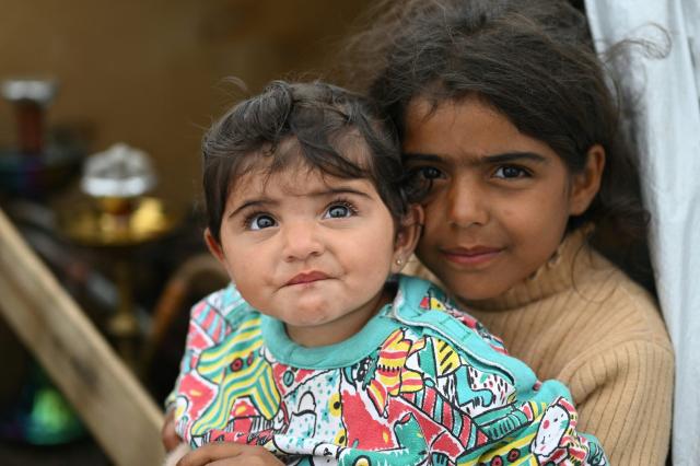 A displaced girl holds her sister as they sit at the entrance of a tent at an unofficial camp for displaced people on Beirut's waterfront area on April 2, 2026. Lebanon was drawn into the Middle East war on March 2 when Tehran-backed militant group Hezbollah launched attacks on Israel to avenge the killing of the Iranian leader. Israel has responded with broad strikes across Lebanon and a ground offensive. (Photo by Joseph EID / AFP)