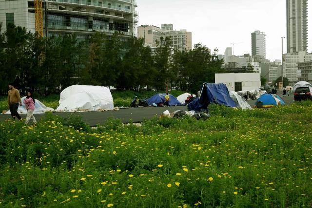 Displaced people walk past their tents at an unofficial camp for displaced people on Beirut's waterfront area on April 2, 2026. Lebanon was drawn into the Middle East war on March 2 when Tehran-backed militant group Hezbollah launched attacks on Israel to avenge the killing of the Iranian leader. Israel has responded with broad strikes across Lebanon and a ground offensive. (Photo by Joseph EID / AFP)