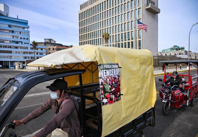 A Cuban on an electric tricycle decorated with a picture of late Cuban President Fidel Castro ride past the US embassy during the anti-imperialist youth march in Havana on April 2, 2026. (Photo by YAMIL LAGE / AFP)