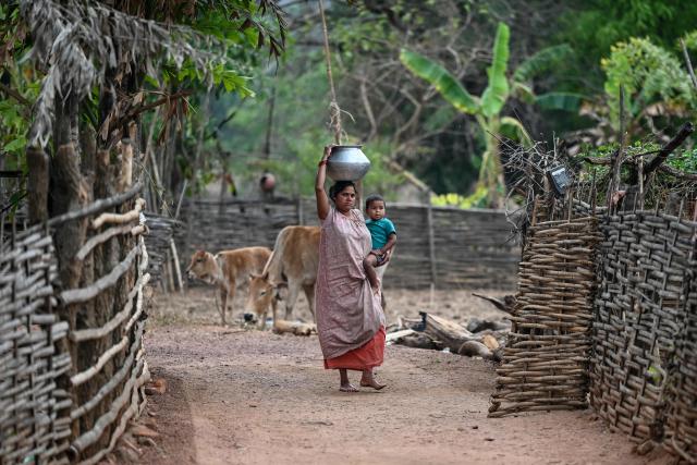 A woman holds a child as she walks along an unpaved road in Mohandi village in Chhattisgarh on April 2, 2026. (Photo by Shammi MEHRA / AFP)