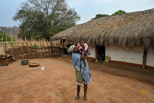 A woman holds a child as she stands outside her hut in Mohandi village in Chhattisgarh on April 2, 2026. (Photo by Shammi MEHRA / AFP)