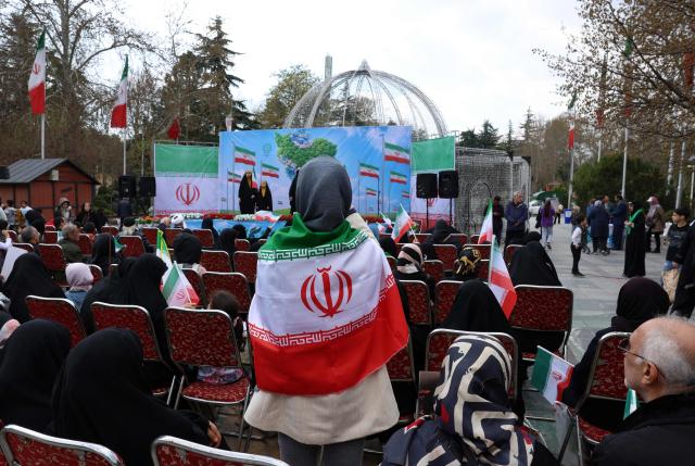 An Iranian woman wearing Iran's flag gathers with others in front of Tehran's Mellat park on April 2, 2026, during "Sizdeh Bedar" (Nature Day), the 13th day after the Nowruz Persian New Year, when people traditionally picnic outdoors with family and friends. Iran on April 2, threatened "crushing" attacks on the US and Israel, firing missiles at Tel Aviv after the US president vowed to bomb the Islamic republic "back to the Stone Ages". (Photo by AFP) / 