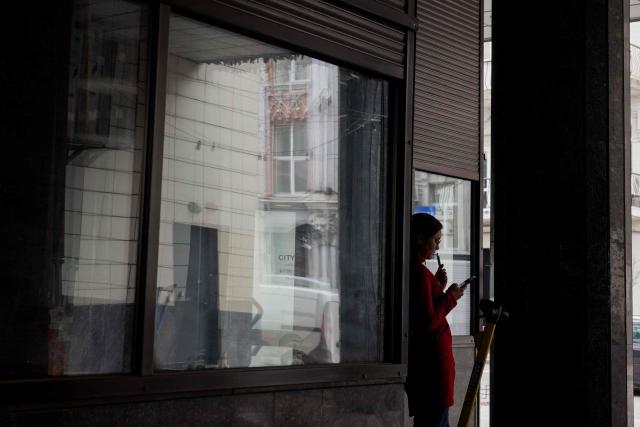 A woman checks her phone whilst vaping under a porch on a street in Kyiv on April 2, 2026, amid the Russian invasion of Ukraine. (Photo by Tetiana DZHAFAROVA / AFP)