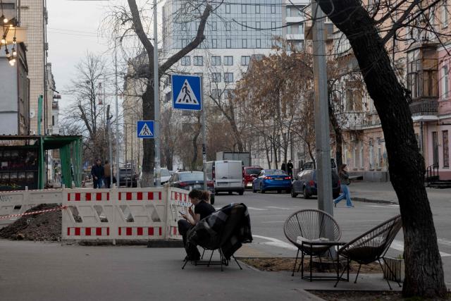 A woman sits on a chair outside a coffee shop in Kyiv on April 2, 2026, amid the Russian invasion of Ukraine. (Photo by Tetiana DZHAFAROVA / AFP)
