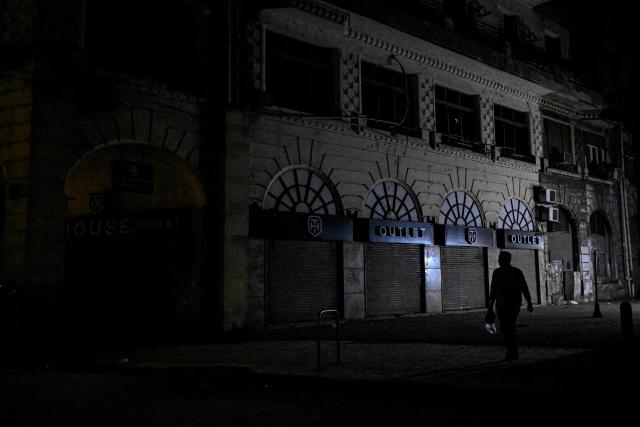 A person walks past shops closed early under a government-ordered curfew aimed at reducing energy costs in downtown Cairo on April 2, 2026. Egypt has ordered shops, restaurants and shopping malls to close from 9:00 pm from April 3, hoping to curb energy bills that have more than doubled because of the Iran war. Prime Minister Mostafa Madbouly announced the curfew and said it would last for a month initially. (Photo by Khaled DESOUKI / AFP)