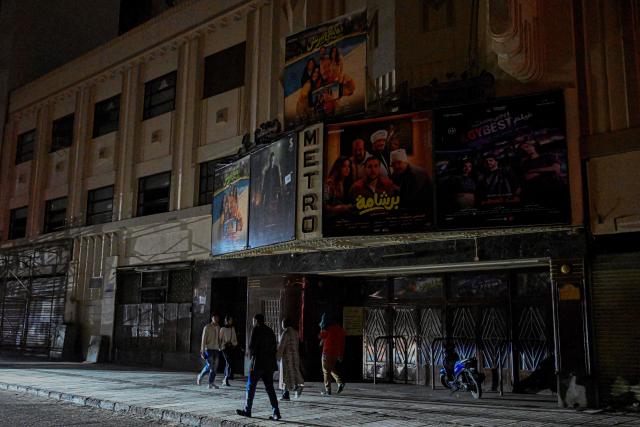 People walk past a closed cinema as shops close early under a government-ordered curfew aimed at reducing energy costs in downtown Cairo on April 2, 2026. Egypt has ordered shops, restaurants and shopping malls to close from 9:00 pm from April 3, hoping to curb energy bills that have more than doubled because of the Iran war. Prime Minister Mostafa Madbouly announced the curfew and said it would last for a month initially. (Photo by Khaled DESOUKI / AFP)