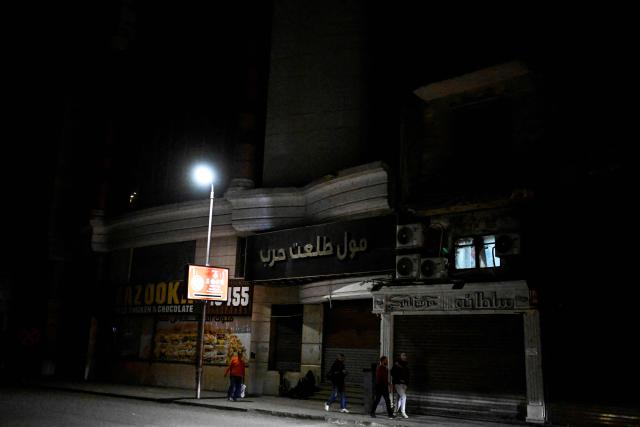 People walk past shops closed early under a government-ordered curfew aimed at reducing energy costs in downtown Cairo on April 2, 2026. Egypt has ordered shops, restaurants and shopping malls to close from 9:00 pm from April 3, hoping to curb energy bills that have more than doubled because of the Iran war. Prime Minister Mostafa Madbouly announced the curfew and said it would last for a month initially. (Photo by Khaled DESOUKI / AFP)