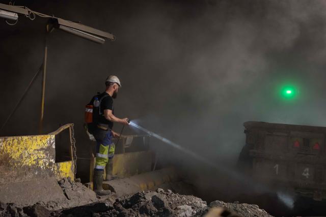 A miner assists in unloading copper ore above a conveyor belt more than 1,000 meters underground in the Polkowice–Sieroszowice copper and silver mine in southwestern Poland, owned by the KGHM conglomerate, a metallurgical powerhouse in the country, on March 25, 2026. Thousands of meters beneath the ground, amid suffocating heat, lies one of the keys to Poland's rumbling mining sector -- and the world economy. (Photo by Wojtek RADWANSKI / AFP)