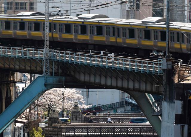 A train passes over a cherry tree growing near a bridge in Tokyo on April 3, 2026. (Photo by ANDREW CABALLERO-REYNOLDS / AFP)