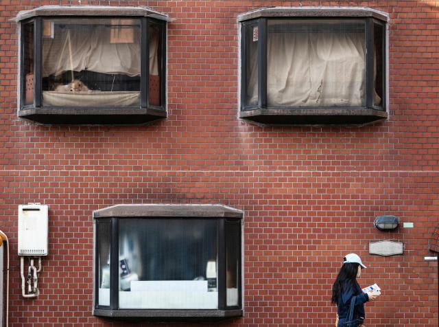 A dog looks out of a window as a woman walks past early in the morning in Tokyo on April 3, 2026. (Photo by ANDREW CABALLERO-REYNOLDS / AFP)