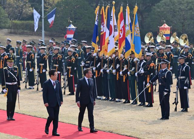 French President Emmanuel Macron (R) and South Korean President Lee Jae Myung (2nd L) inspect honour guards during the welcome ceremony at the presidential Blue House in Seoul on April 3, 2026. (Photo by JUNG YEON-JE / POOL / AFP)