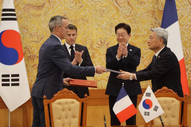French President Emmanuel Macron (back-L) and South Korean President Lee Jae-myung (back-R) witness Nicolas Maes (L), CEO of French nuclear firm Orano, and Kim Hoe-chun (R), CEO of South Korea Hydro and Nuclear Power, exchange documents during a signing ceremony of agreements in Seoul on April 3, 2026. (Photo by Ludovic MARIN / AFP)