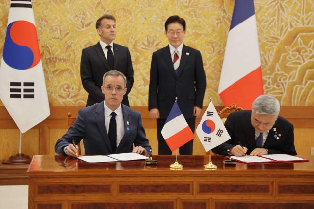 French President Emmanuel Macron (back-L) and South Korean President Lee Jae-myung (back-R) witness Nicolas Maes (L), CEO of French nuclear firm Orano, and Kim Hoe-chun (R), CEO of South Korea Hydro and Nuclear Power, sign documents during a signing ceremony of agreements in Seoul on April 3, 2026. (Photo by Ludovic MARIN / AFP)