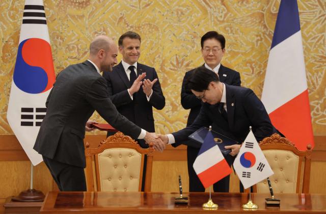 French President Emmanuel Macron (back-L) and South Korean President Lee Jae-myung (back-R) witness Jean-Noel Barrot, French Minister for Europe and Foreign Affairs, and Kim Jung-kwan, Minister of Trade, Industry and Resources, exchange documents during a signing ceremony of agreements in Seoul on April 3, 2026. (Photo by Ludovic MARIN / AFP)
