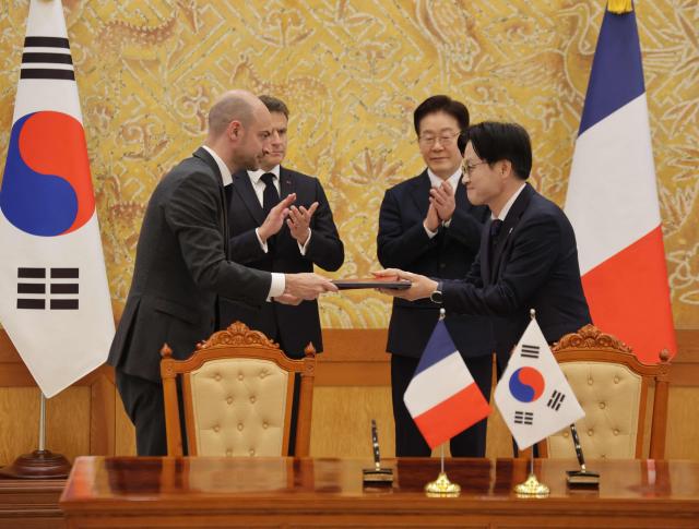 French President Emmanuel Macron (back-L) and South Korean President Lee Jae-myung (back-R) witness Jean-Noel Barrot, French Minister for Europe and Foreign Affairs, and Kim Jung-kwan, Minister of Trade, Industry and Resources, exchange documents during a signing ceremony of agreements in Seoul on April 3, 2026. (Photo by Ludovic MARIN / AFP)