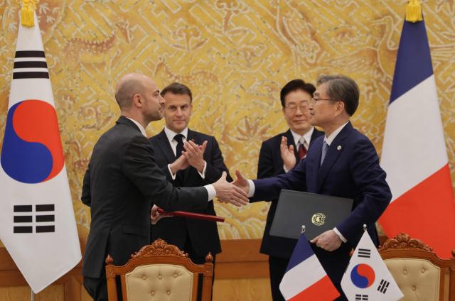 French President Emmanuel Macron (back-L) and South Korean President Lee Jae-myung (back-R) witness Jean-Noel Barrot, French Minister for Europe and Foreign Affairs, and South Korea's Foreign Minister Cho Hyun, exchange documents during a signing ceremony of agreements in Seoul on April 3, 2026. (Photo by Ludovic MARIN / AFP)