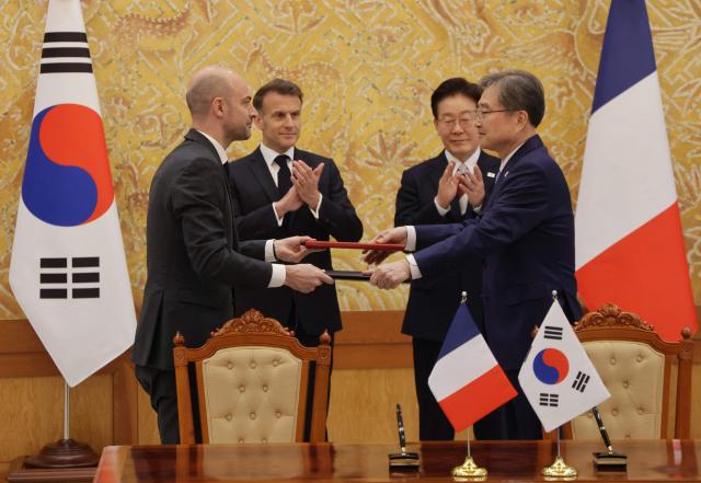 French President Emmanuel Macron (back-L) and South Korean President Lee Jae-myung (back-R) witness Jean-Noel Barrot, French Minister for Europe and Foreign Affairs, and South Korea's Foreign Minister Cho Hyun, exchange documents during a signing ceremony of agreements in Seoul on April 3, 2026. (Photo by Ludovic MARIN / AFP)