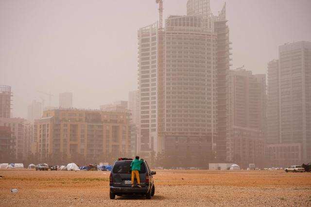 TOPSHOT - A displaced boy stands on the back of a car at an unofficial camp erected along Beirut's seafront area during a sandstorm on April 3, 2026. Lebanon was drawn into the Middle East war on March 2 when Tehran-backed militant group Hezbollah launched attacks on Israel to avenge the killing of the Iranian leader. Israel has responded with broad strikes across Lebanon and a ground offensive. (Photo by Dimitar DILKOFF / AFP)