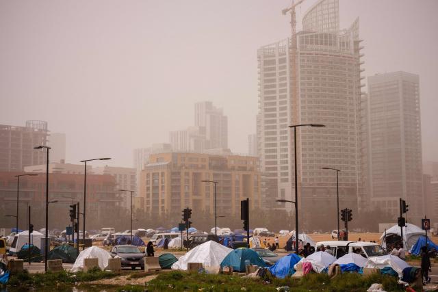 Displaced families stand next to their tents at an unofficial camp erected along Beirut's seafront area during a sandstorm on April 3, 2026. Lebanon was drawn into the Middle East war on March 2 when Tehran-backed militant group Hezbollah launched attacks on Israel to avenge the killing of the Iranian leader. Israel has responded with broad strikes across Lebanon and a ground offensive. (Photo by Dimitar DILKOFF / AFP)