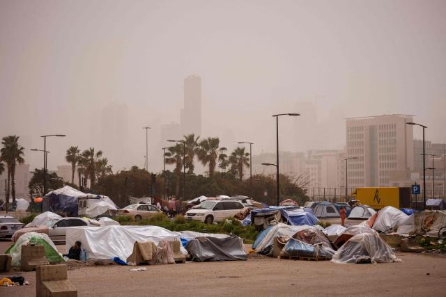 Displaced people rest outside their tents at an unofficial camp erected along Beirut's seafront area during a sandstorm on April 3, 2026. Lebanon was drawn into the Middle East war on March 2 when Tehran-backed militant group Hezbollah launched attacks on Israel to avenge the killing of the Iranian leader. Israel has responded with broad strikes across Lebanon and a ground offensive. (Photo by Dimitar DILKOFF / AFP)