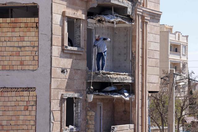 A man holds a bucket with a rope on a residential building that was damaged by recent strikes at Vahdat town in Karaj, southwest of Tehran on April 3, 2026. Iran and its allies traded fire with Israel and the United States, as Washington-linked assets across the Middle East were targeted alongside civilian infrastructure -- with the month-long war on April 3 showing little sign of easing. (Photo by ATTA KENARE / AFP) / 