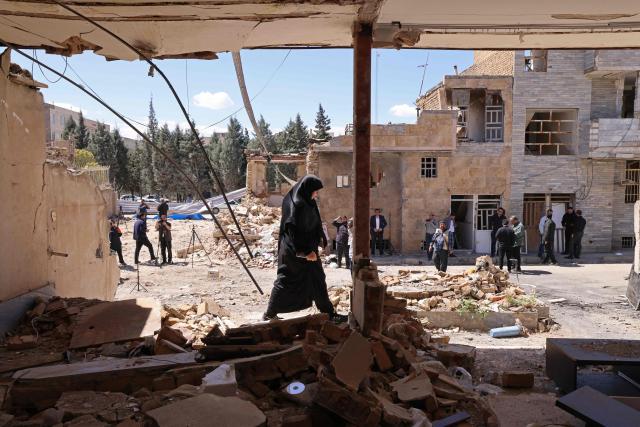A woman walks past the residential buildings that were damaged by recent strikes at Vahdat town in Karaj, southwest of Tehran on April 3, 2026. Iran and its allies traded fire with Israel and the United States, as Washington-linked assets across the Middle East were targeted alongside civilian infrastructure -- with the month-long war on April 3 showing little sign of easing. (Photo by ATTA KENARE / AFP) / 